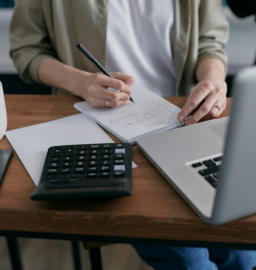 Calculating bills, with a calculator on the desk and a laptop crunching the numbers on a note pad on Med Pay Coverage.